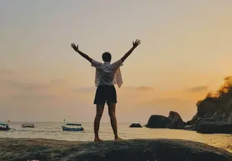 Standing, arms extended, facing the sunset over the beach in southern Goa.