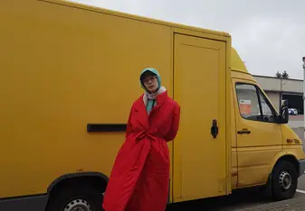William is standing outside in bright winter clothes in front of a small, yellow truck.
