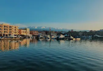 Crete, Greece is one of the most beautiful islands. One of the most recognized places on the island is Chania, where there is a long pier along the ocean with small shops and restaurants. You can also see the snow covered mountains in the distance showing the diversity of the country.