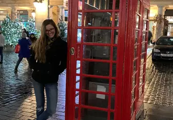 a student leaning against a red phone booth and smiling