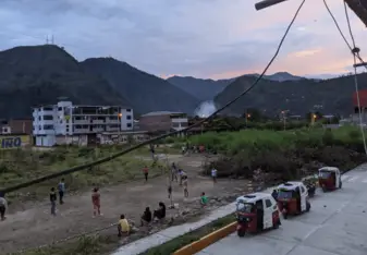 a Peruvian village at sunset, buildings in the background, a few villagers playing football in the foreground
