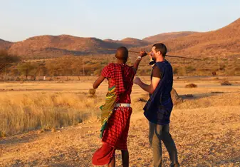 a white man and a Maasai man standing in the savannah