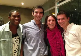 four people smiling at the camera with their arms around each others' shoulders