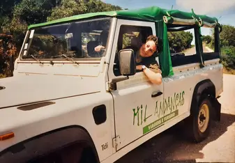 A smiling woman peering through the window of a Jeep