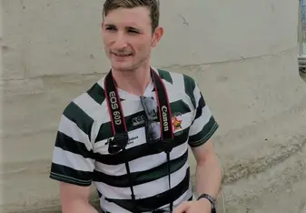 a young man leaning against a wall, holding a camera