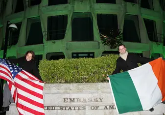 two people posing with Irish and American flags outside of a US Embassy