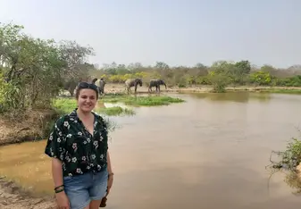 Libby posing in front of a lake with elephants in the background