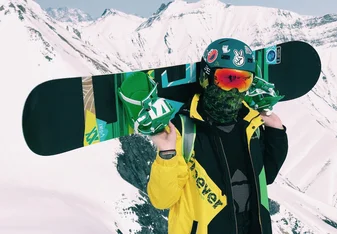 Snowboarder holding board in green and yellow jacket with helmet