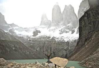 student throwing their arms up while standing on a rock with a vast mountain landscape behind them