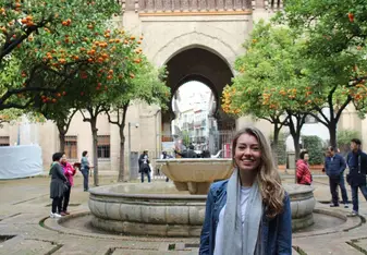 A woman in Spain posing with orange trees in the background.