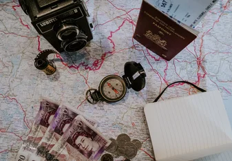 A camera, compass, passport, journal and currency on top of a map