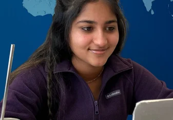 young woman smiling at computer with glass of water and a straw beside her and a virtual world behind her