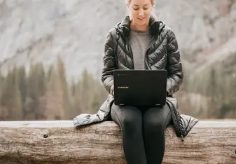 Person sitting on tree log while using laptop
