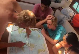 Three teens and instructor in sailboat planning passage on map