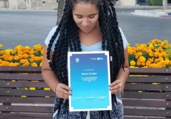 Woman with long black twists looking down at a certificate she's holding up to the camera