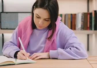 Person sitting at table writing in notebook 