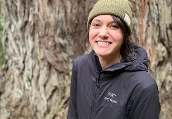 Amy Krzyzek standing in front of a tree wearing a green beanie and black Arcteryx jacket smiling 