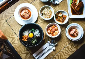 Several bowls on a table with various Korean foods in them.