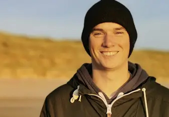 Niall Coombes wearing a black beanie and black zip up jacket smiling 