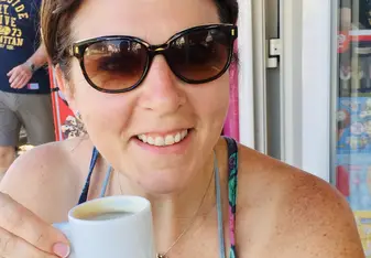 Onora Gill-Fitch holding an espresso and smiling while wearing sunglasses