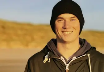 Niall Coombes wearing a black beanie and black zip up jacket smiling 