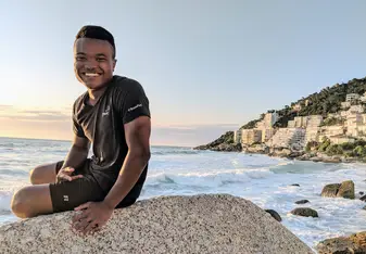 Alfred sitting on a boulder at the beach in South Africa smiling