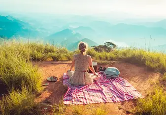 Woman sitting alone on picnic blanket facing the mountains.