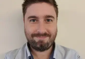 Jacob Thomas with short brown hair, a beard, and a button down shirt