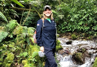Vanessa Rees standing in a stream in a jungle with a hat on smiling