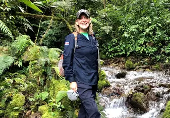 Vanessa Rees standing in a stream in a jungle with a hat on smiling