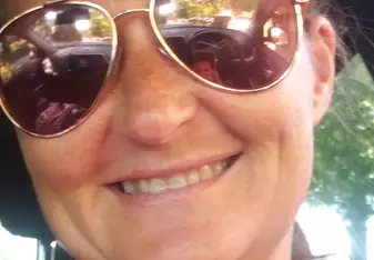 Amanda Collins wearing sunglasses and a pink shirt smiling