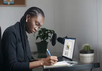 A person sitting in front of a computer while writing in a journal