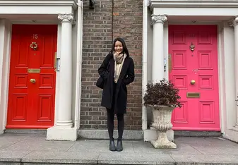 A person standing in front of two residential doors, one red and one pink