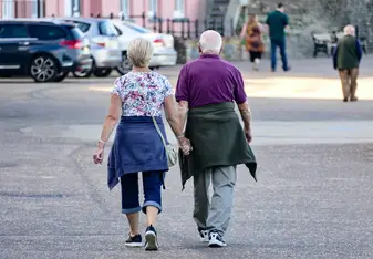 Two older adults holding hands walking down a street