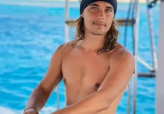 Joma Dix with long hair steering a boat wearing a beanie 
