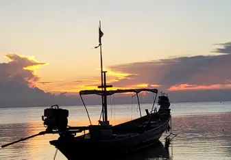 A boat on the ocean with the sun setting behind it
