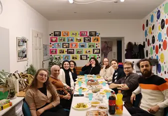 A large group poses for a photo while sitting around a table with food on their plates.
