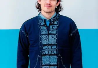 William Davies wearing a blue traditional shirt and navy cardigan with long brown hair and blue eyes