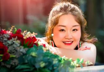 Cong Meng with brunette hair and red lipstick smiling with her head resting on her arms
