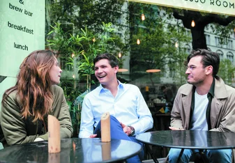 One female and two male postgraduate students sit at a table outside a cafe