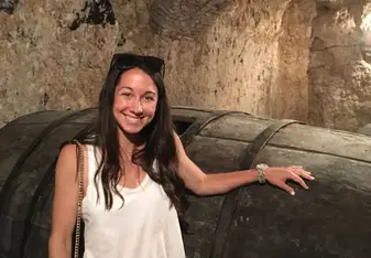 Brittany Shelley in a wine cellar wearing a white tank top, with dark hair, and sunglasses smiling