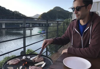 SJ Vermaak grilling food wearing sunglasses on a dock by a river