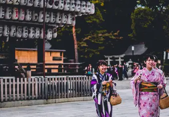 Women dressed in traditional Japanese clothing stand and smile outside.
