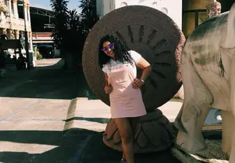 Kirsty Davids with sunglasses on and a pink overall dress smiling