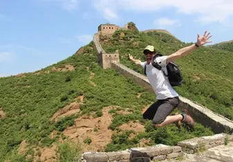 A man jumps in the air smiling on the Great Wall of China.