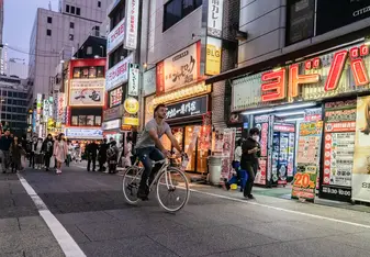 A man rides a bicycle through a busy Japanese street.