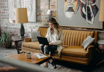 A woman on a laptop sits on a couch.