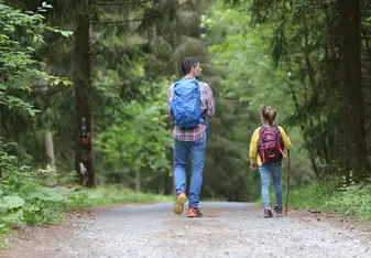 A man and little girl hike in the woods.