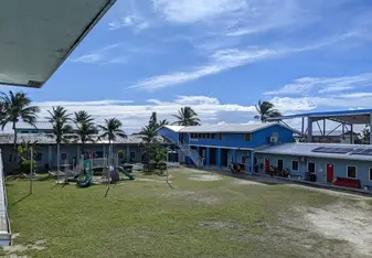 Large green field with play structure to the left.  Two blue wings of the school create a corner focus point under a blue sky.