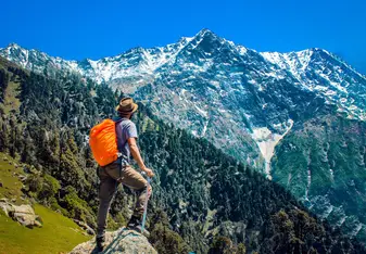 A man stands facing a valley and mountains.